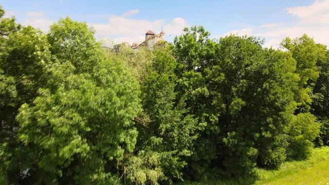 Cinematic aerial drone shot revealing the church and fortress on the hill behind trees in the town of Aarburg in Switzerland