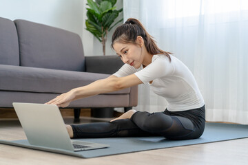 Fototapeta premium Fit, sporty asian young beautiful woman, girl doing physical or pilates, watching trainer online on laptop computer, training in living room.Workout fitness exercise people in sportswear at home.