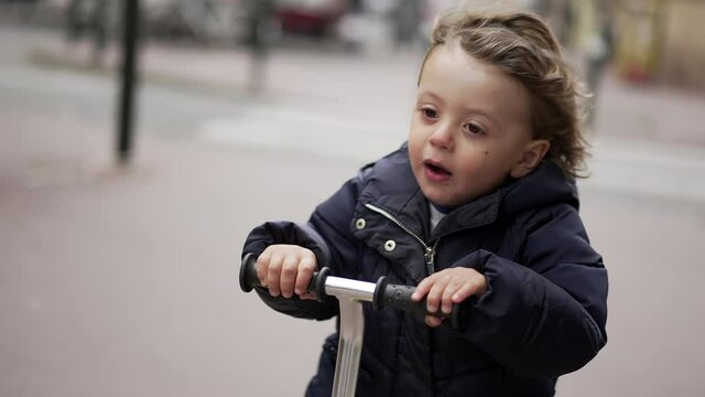 Happy little todder riding scooter in urban sidewalk street