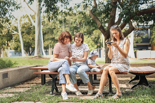 Three women friends with baby strollers reading text message in park