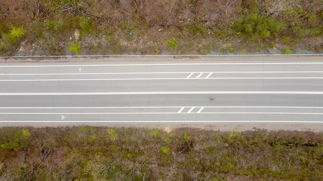 View from above. The athlete runs along an empty asphalt road among a low forest. Running marathon.