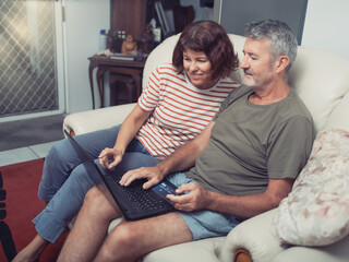 Smiling middle aged couple sitting on their couch using the laptop to buy online at home
