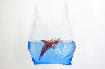 Fototapeta na wymiar Plastic bag holding blurred dolphin toy model in water surface on white background. Minimal world ocean day concept.