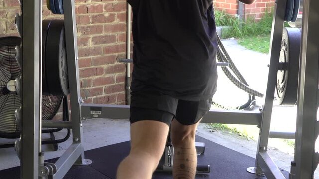 Muscly man in home gym exercising shot from back calf raise smith machine