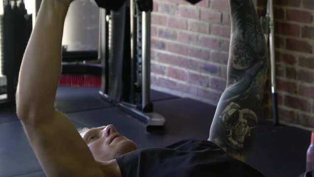 Tattooed muscly man in home gym working out close up inward tricep press