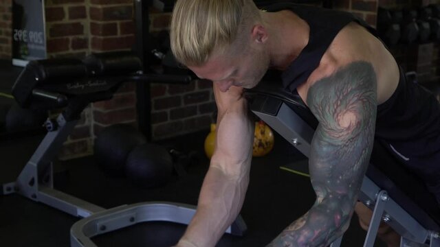 Tattooed muscly man in home gym working out goblet bicep curl