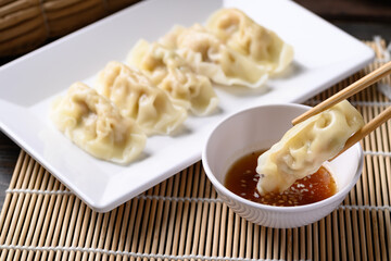 Steamed wonton dumpling stuffed with minced pork and shrimp on plate eating with sesame oil sauce by chopsticks, Asian cuisine