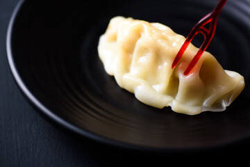 Close up of steamed wonton dumpling on black dish eating by red fork, Asian food