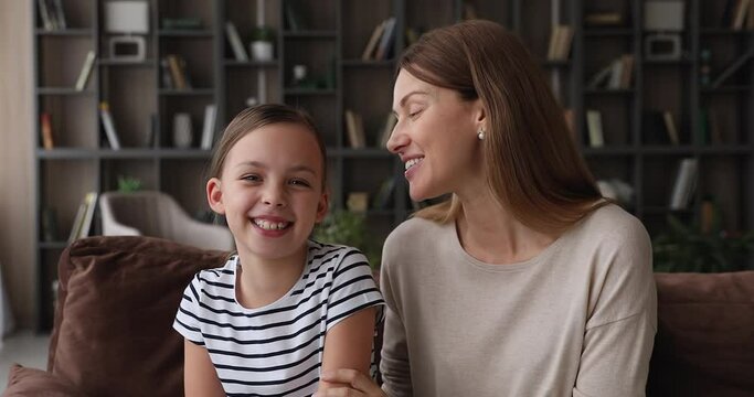 Mom and little daughter sit on sofa at home looking at camera laughing enjoy pleasant remote conversation use videoconferencing app. Virtual meeting with family, modern tech, video call event concept