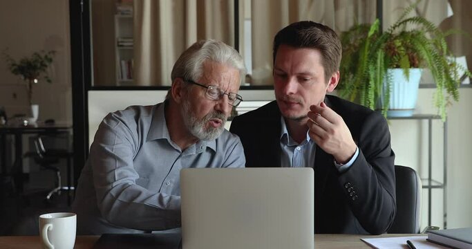 Focused middle aged mature hoary leader boss looking at computer screen, working on project with motivated young male colleague, discussing presentation, analyzing online sales or services in office.