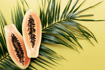 Fresh tropical papaya fruit halves on the palm leaf on a yellow background