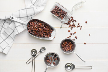 Composition of scoop and pot with coffee beans on light wooden background