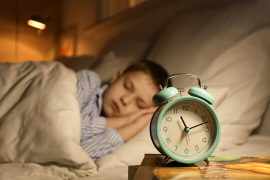 Alarm clock on table of sleeping little boy in bedroom