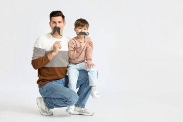 Happy father and his little son with party decor on light background