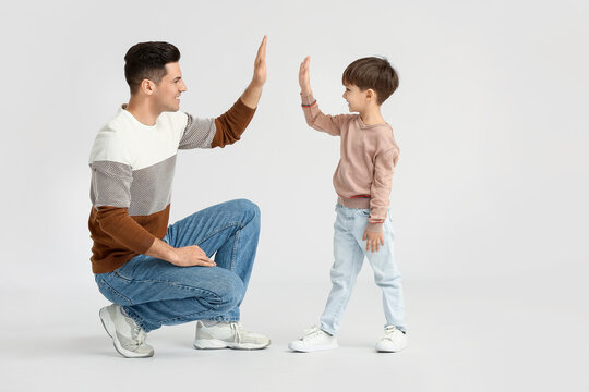 Happy father and his little son giving each other high-five on light background