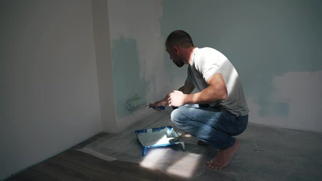Caucasian man paints the wall with a brush Dad makes repairs in the room Quality work Side view