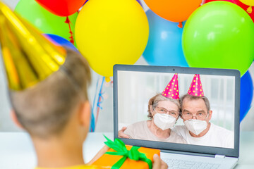 Obraz na płótnie Canvas Young boy wearing party's cap celebrating birthday with his grandparents on video call during the coronavirus epidemic