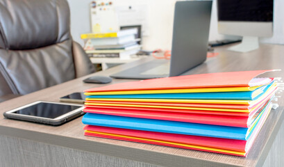 Colorful folders of data report documents stack on manager table with blurred office equipment...