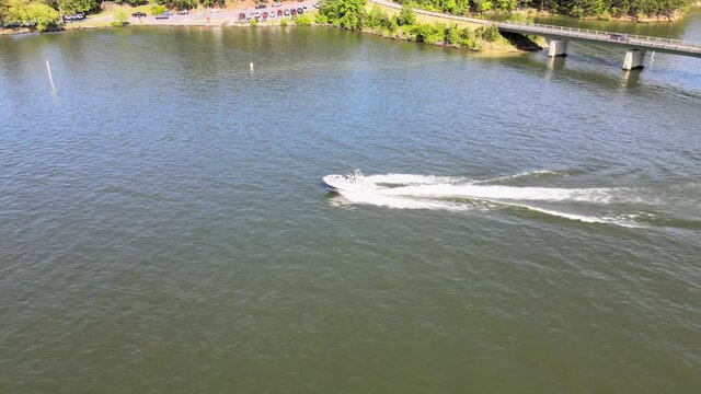 V-Hull Ski boat throttling up from no wake zone and cruising on lake. Camera moves parallel to the vessel