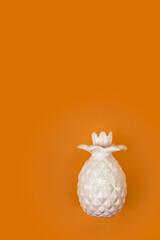 Decorative ceramic white pineapple on a bright orange background. Pineapple on an orange background, trending color.