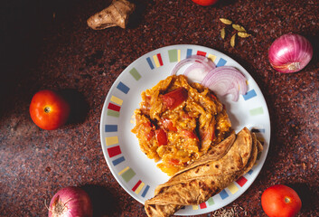Freshly prepared eggplant in traditional spices served with Indian bread. Flat lay of north Indian spicy brinjal on a kitchen slab with fresh ingredients decorated around it.