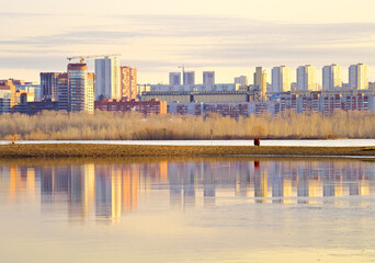 Fototapeta na wymiar Morning on the Ob River in Novosibirsk. The high-rise buildings of the new residential area stand on the shore in the morning golden light, reflected in the water. Siberia, Russia