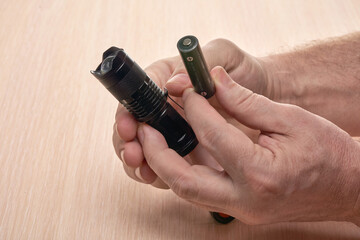 Hands hold a small black flashlight and replace the battery in it