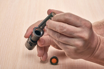 Hands hold a small black flashlight and replace the battery in it