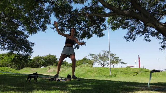 Young woman balance and fall of slack line and laughs at the park in a sunny day