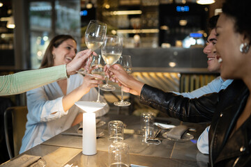 Multiracial young people toasting with wineglasses up at restaurant.