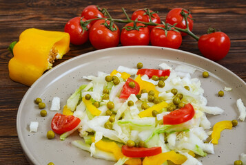 fresh summer vegetable salad with peking cabbage, cherry tomatoes, green peas and yellow bell pepper on a ceramic plate