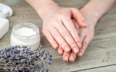 Women's hands in the process of spreading cream and a jar of natural cream on a wooden table....