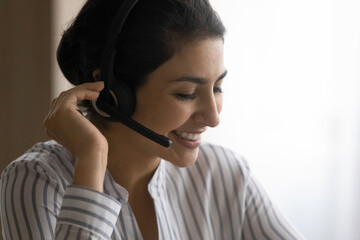 Close up smiling Indian woman manager agent in wireless headset microphone consulting customer by...