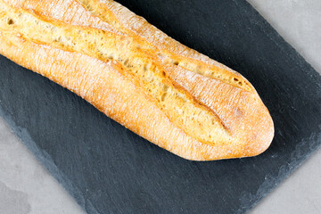 french baguette bread on black cutting board on grey concrete background. Diagonal.