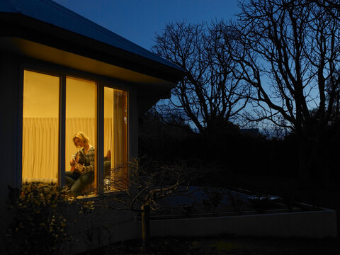 Teenage girl playing guitar inside home in the evening