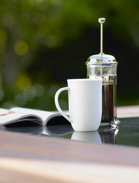 Plunger of coffee, cup and magazine on outdoor table setting