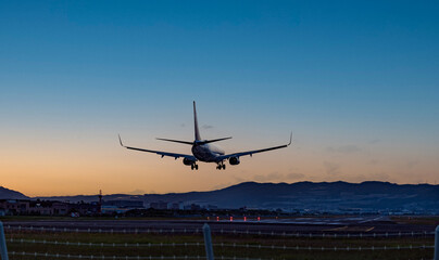 Fototapeta na wymiar 夕焼けをバックに着陸する飛行機のシルエット 