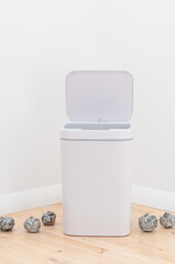 Smart waste basket. Electronic gadget for the home. The lid opens and closes automatically. Nearby is crumpled paper. On a wooden floor. The background is white.