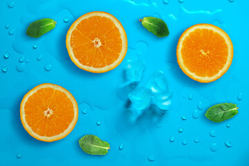Fresh juicy slices of orange and mint leaves on bright blue background covered with water drops. Creative food background, top view