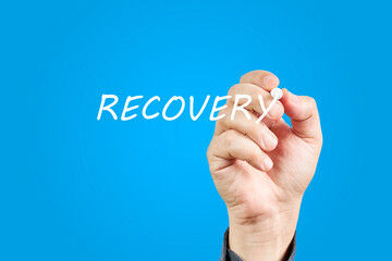 Hand of man writing the word Recovery on a blue background