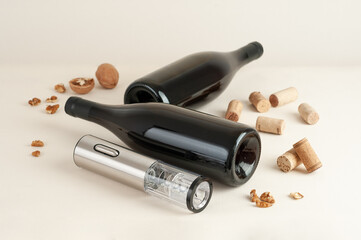 Electric corkscrew made of metal. Nearby are two bottles, corks and walnuts. Light background.
