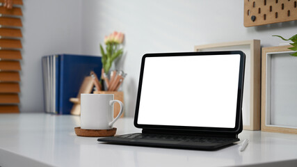 Mock up computer tablet with blank screen, coffee cup and supplies on white desk.