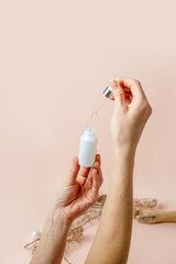 Cropped view of woman holding pipette with serum in hand on beige trendy neautral earth tones background. Beauty cosmetic product for skincare concept, copy space, beauty salon flyer