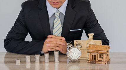 A pile of coins and house clocks on a desk businessman money saving idea house name