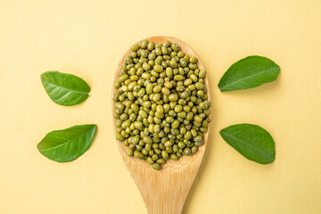 Portion of green beans in a wooden spoon on a yellow table with leaves. Concept of proper balanced nutrition and healthy food