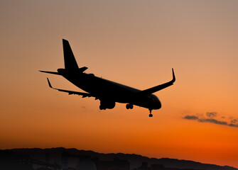 Fototapeta na wymiar 夕陽を背景に着陸態勢に入る飛行機のシルエット