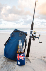 Beer in stubbie holder with Australian Flag, cooler bag and fishing rod on the beach on Australia Day