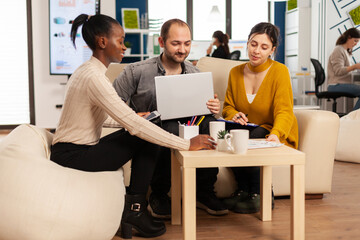 Startup team meeting with company leader pointing at strategy on financial reports. Team work in modern office of diverse international colleagues group sitting on couch at table in startup management