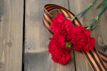 bouquet of red carnations with a St. George ribbon on a wooden background. Georgievsk ribbon - Russian symbol of victory and three red carnations. Holiday card for the holiday of May 9.