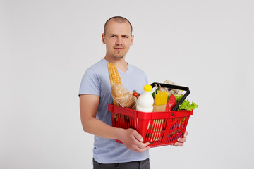 Obraz na płótnie Canvas young man with shopping basket full of products posing over white